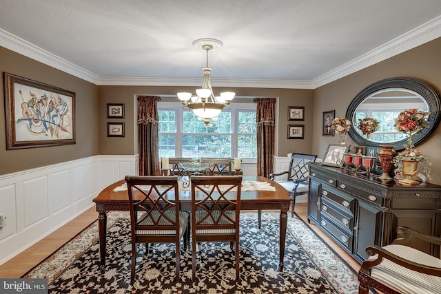 dining space with light wood-style flooring, a textured ceiling, a notable chandelier, and wainscoting