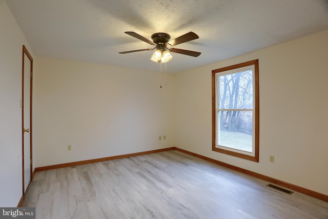 spare room with light wood-style floors, baseboards, visible vents, and a textured ceiling