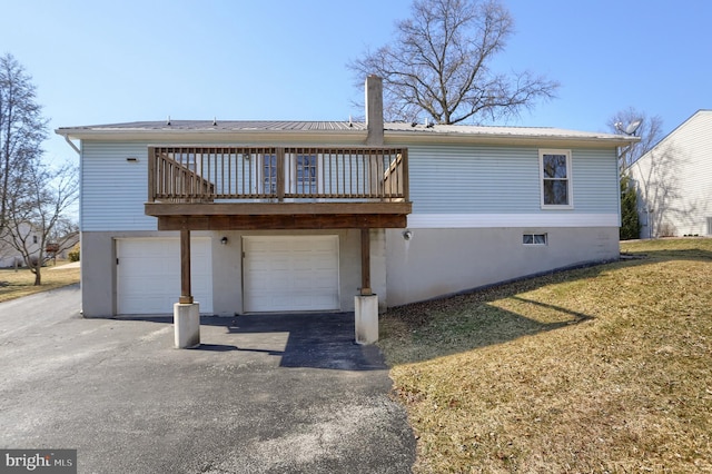 rear view of property featuring metal roof, aphalt driveway, a garage, a yard, and a wooden deck