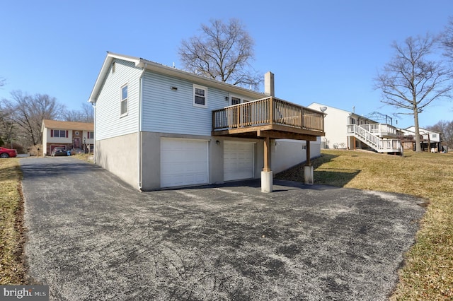 rear view of property with aphalt driveway, a garage, a yard, a wooden deck, and stucco siding