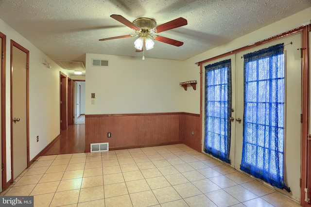 unfurnished room with french doors, visible vents, a textured ceiling, and wainscoting