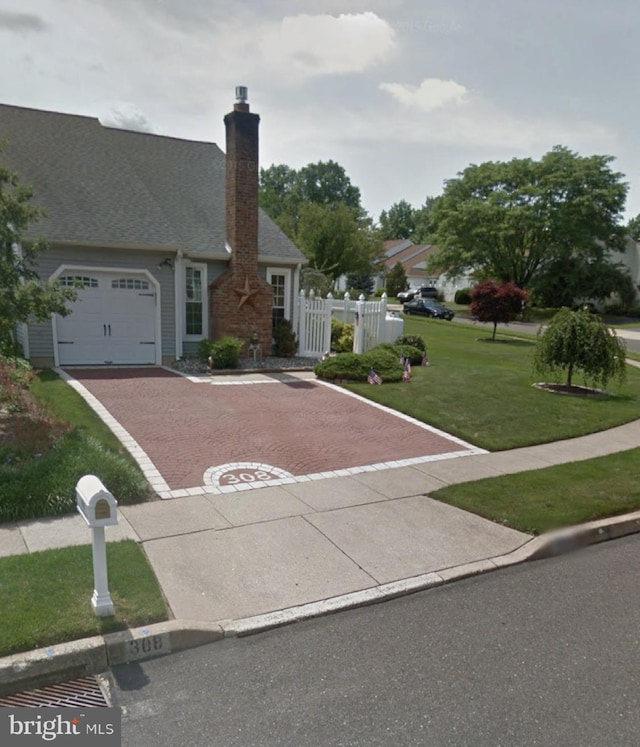 view of front facade featuring a front lawn, decorative driveway, fence, an attached garage, and a chimney