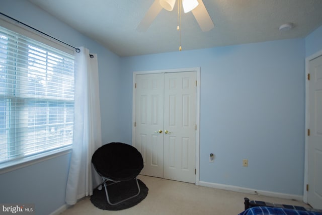 living area with a wealth of natural light, light carpet, ceiling fan, and baseboards