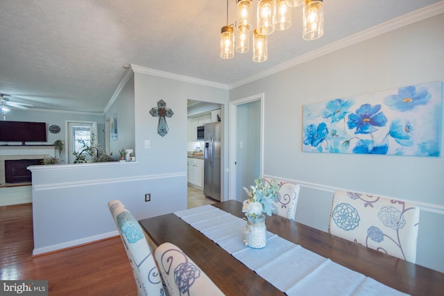 dining area featuring ornamental molding, wood finished floors, a textured ceiling, a fireplace, and ceiling fan with notable chandelier