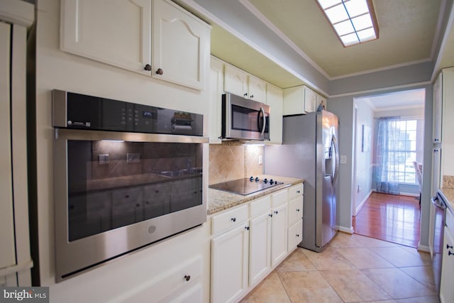 kitchen with light tile patterned floors, stainless steel appliances, white cabinetry, ornamental molding, and backsplash