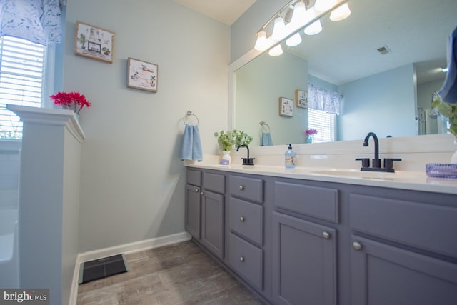 bathroom with double vanity, wood finished floors, a sink, and visible vents