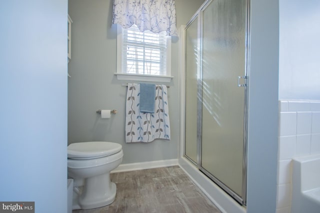 bathroom with a stall shower, baseboards, toilet, wood finished floors, and a washtub