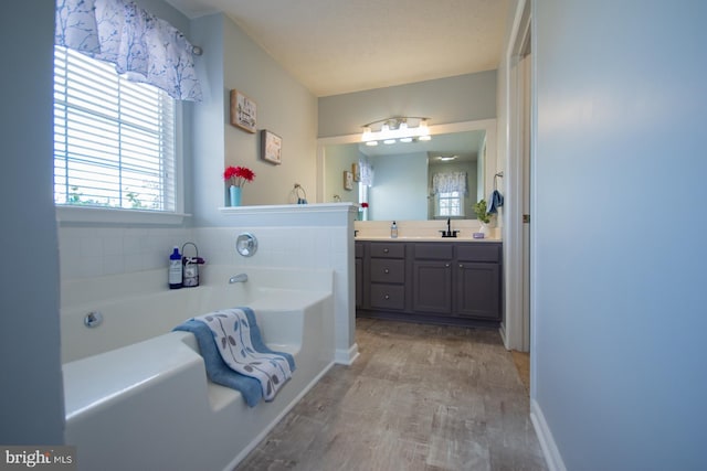 full bath featuring a garden tub, vanity, and wood finished floors