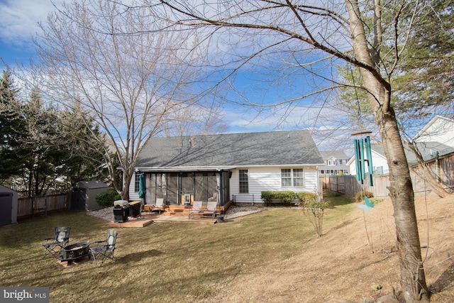 rear view of property with a sunroom, fence, a fire pit, and a shed