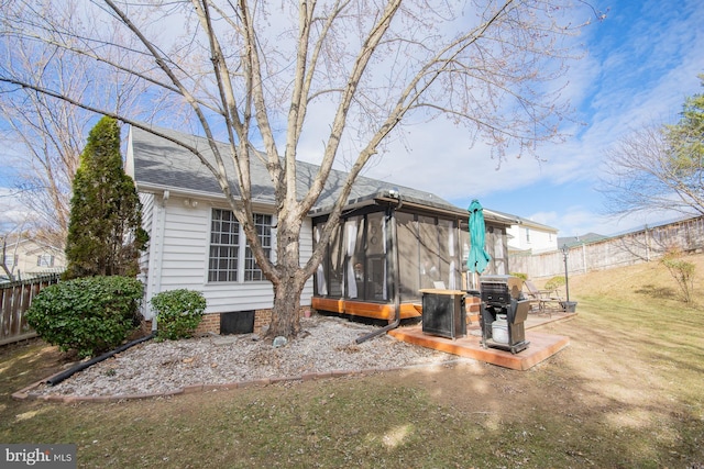 back of property with a shingled roof, a fenced backyard, and a sunroom