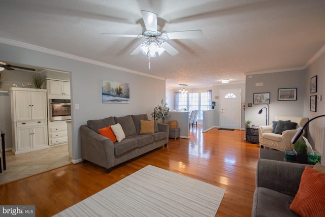 living room with a textured ceiling, a ceiling fan, baseboards, ornamental molding, and light wood-type flooring