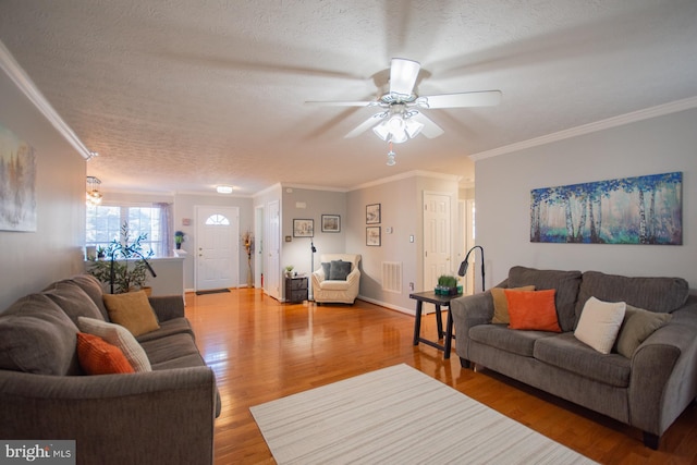 living room featuring a textured ceiling, ornamental molding, wood finished floors, and visible vents