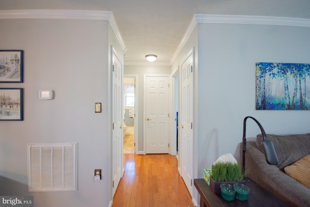 hallway with light wood-style floors, visible vents, and crown molding