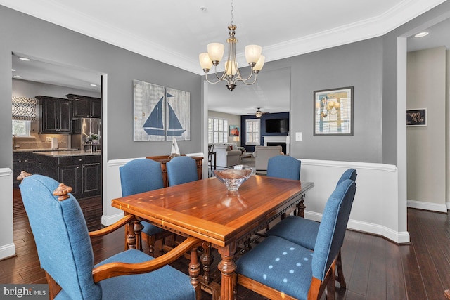 dining room with dark wood-style floors, ornamental molding, ceiling fan with notable chandelier, and a fireplace