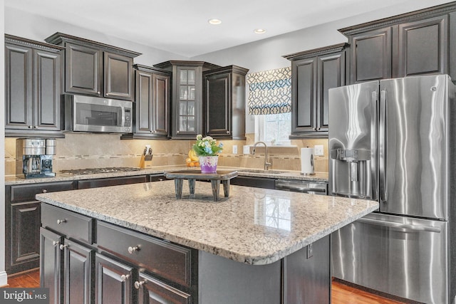 kitchen featuring decorative backsplash, appliances with stainless steel finishes, wood finished floors, a center island, and a sink