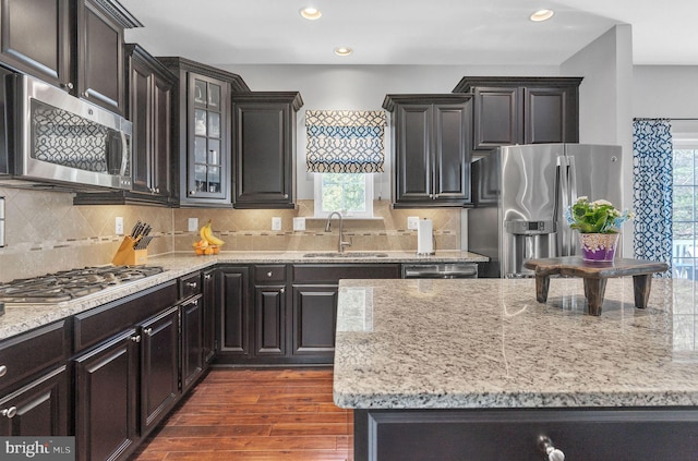 kitchen featuring light stone counters, dark wood-style flooring, a sink, stainless steel appliances, and a wealth of natural light