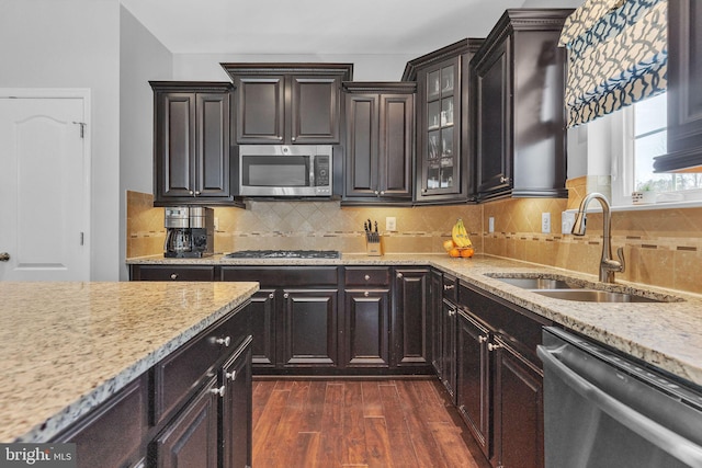 kitchen featuring dark wood finished floors, decorative backsplash, glass insert cabinets, stainless steel appliances, and a sink