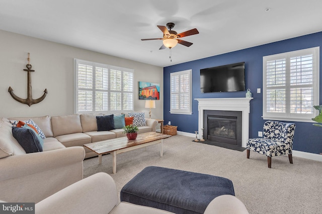 living area featuring carpet, baseboards, a ceiling fan, and a fireplace with flush hearth