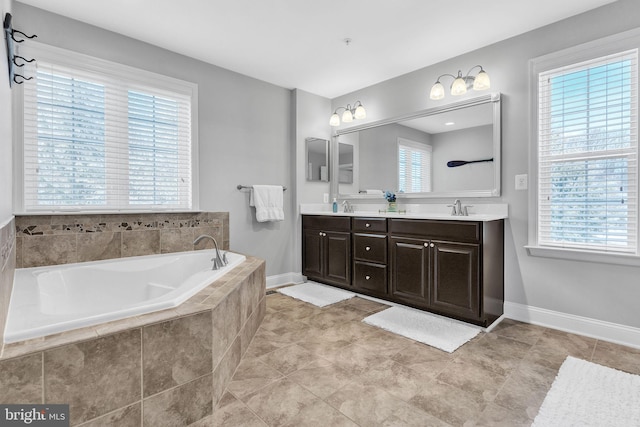 full bathroom with double vanity, a garden tub, baseboards, and a sink