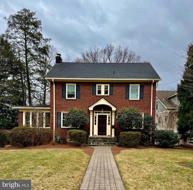 colonial home featuring brick siding, a chimney, and a front yard