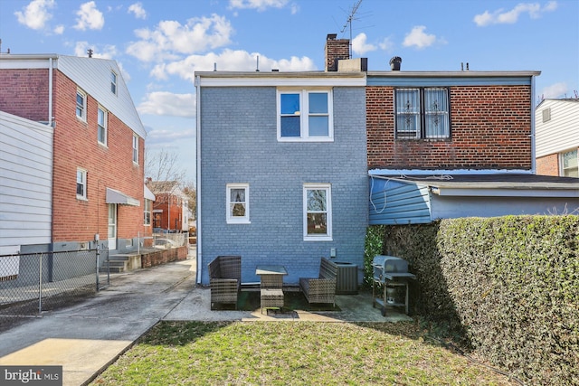 rear view of house with brick siding, a chimney, and fence