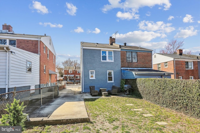 rear view of property featuring a yard, brick siding, a chimney, and fence