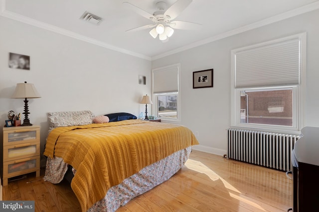 bedroom featuring visible vents, baseboards, radiator heating unit, ornamental molding, and wood finished floors