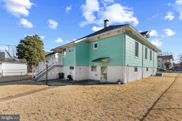 back of property featuring stairway, fence, a yard, central AC, and a chimney