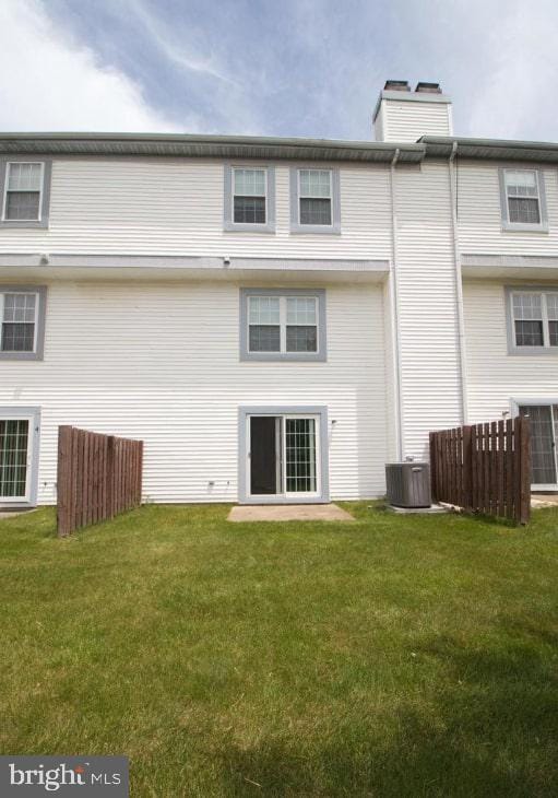 rear view of house featuring central AC unit, a lawn, a chimney, and fence