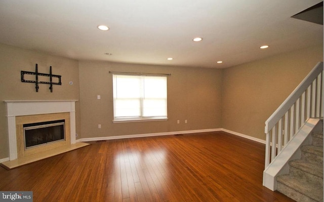 unfurnished living room featuring a high end fireplace, stairway, baseboards, and hardwood / wood-style flooring