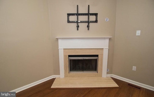 room details featuring a fireplace with flush hearth, visible vents, baseboards, and wood finished floors