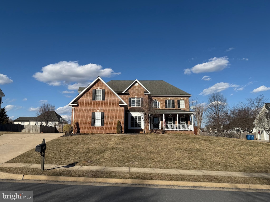 view of front of house with a porch, a front lawn, fence, and brick siding