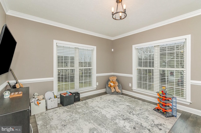 rec room with an inviting chandelier, ornamental molding, baseboards, and wood finished floors