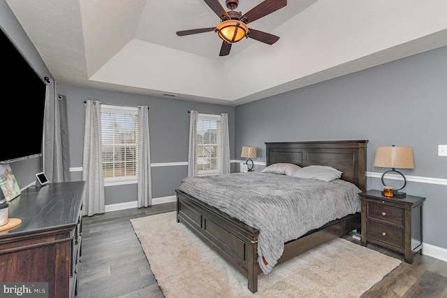 bedroom with a raised ceiling, baseboards, dark wood-style floors, and ceiling fan