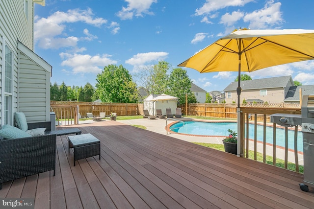 view of pool featuring a wooden deck, an outdoor structure, a fenced backyard, and a storage unit