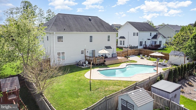 rear view of property with a wooden deck, a fenced in pool, a fenced backyard, a shed, and a yard
