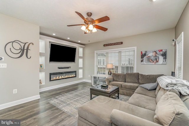 living area featuring a glass covered fireplace, wood finished floors, baseboards, ceiling fan, and recessed lighting