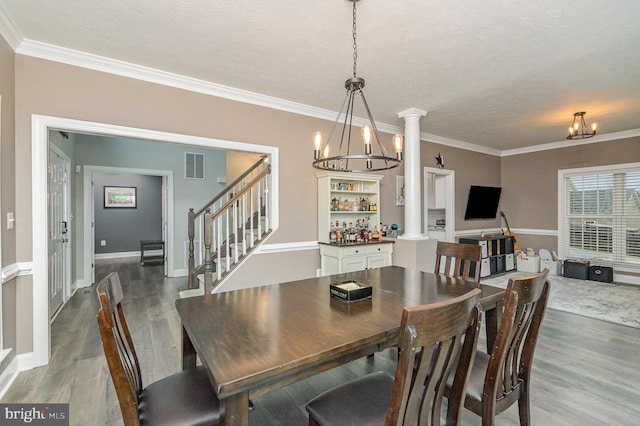 dining space with visible vents, crown molding, wood finished floors, a notable chandelier, and ornate columns