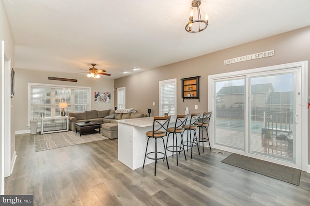 kitchen with baseboards, ceiling fan with notable chandelier, wood finished floors, and a breakfast bar