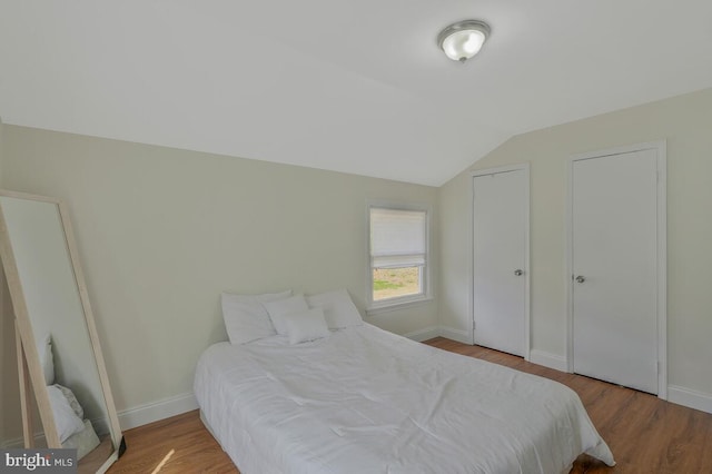 bedroom with wood finished floors, baseboards, and vaulted ceiling