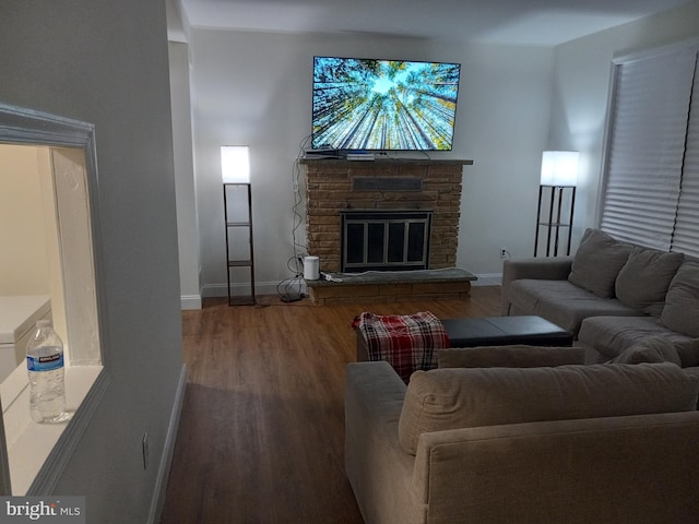 living room featuring a stone fireplace, baseboards, and wood finished floors