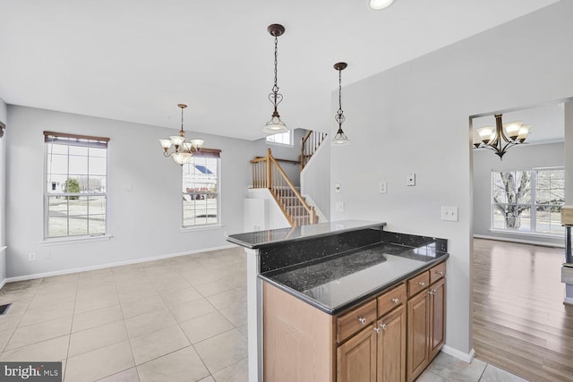 kitchen featuring baseboards, brown cabinetry, dark stone counters, a chandelier, and pendant lighting