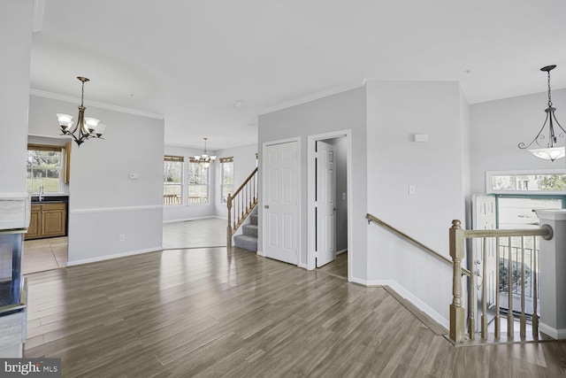 unfurnished living room with baseboards, ornamental molding, light wood-type flooring, and a notable chandelier