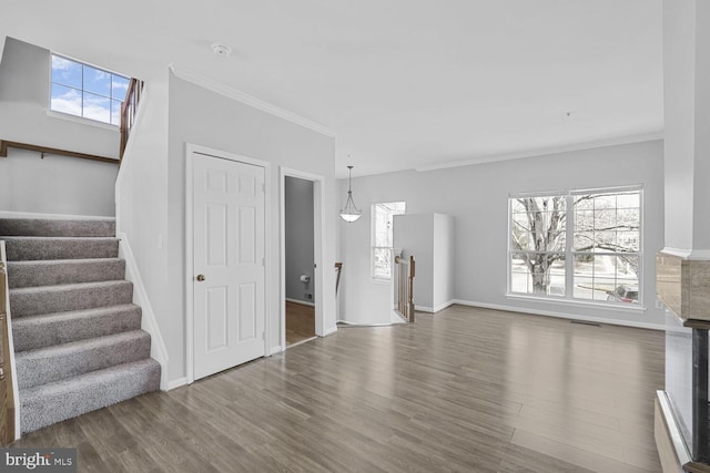 unfurnished living room with a healthy amount of sunlight, crown molding, baseboards, and wood finished floors