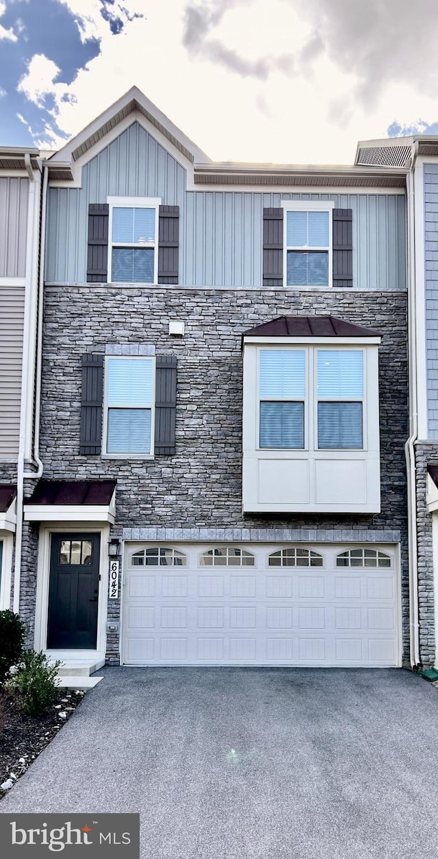 townhome / multi-family property featuring board and batten siding, an attached garage, stone siding, and driveway