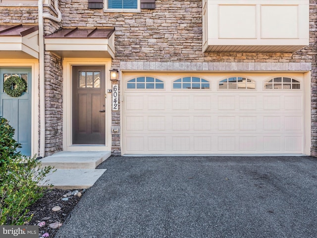 property entrance featuring a garage, stone siding, and driveway