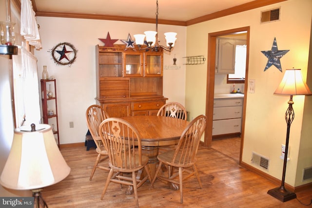 dining area featuring visible vents, crown molding, light wood-style flooring, and an inviting chandelier