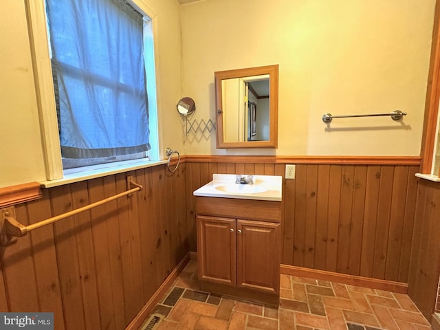 bathroom with brick floor, a wainscoted wall, wood walls, and vanity