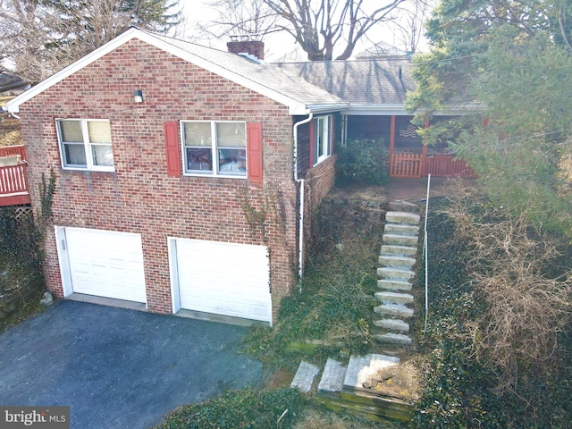 view of side of home with a garage, driveway, brick siding, and a chimney