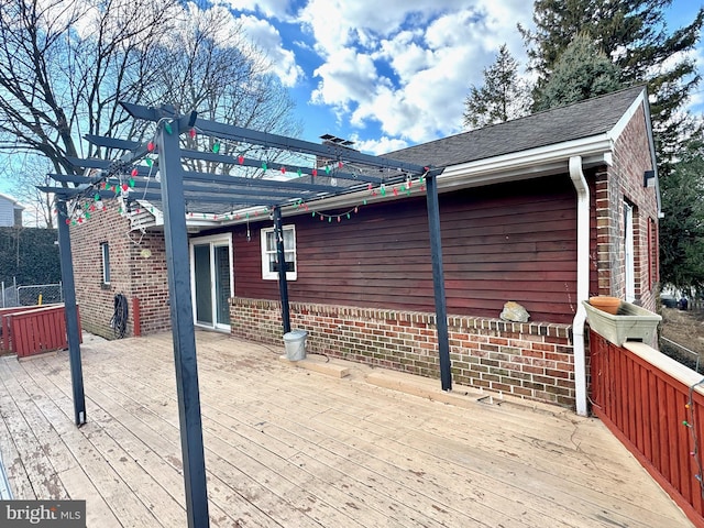 view of property exterior with a shingled roof, brick siding, a deck, and a pergola